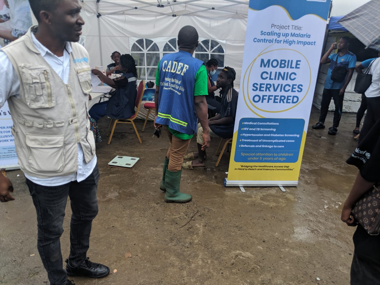 CADEF staff and partner personnel at a mobile-clinic tent with a banner describing available services in Limbe